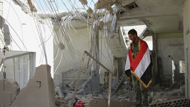 A Syrian soldier wrapped in a Syrian flag stands in a damaged house in Achan, Hama province, Syria, on Sunday.