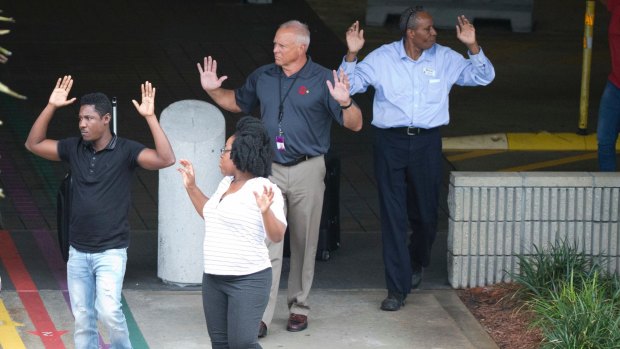 People leave a garage area with their hands up in the air outside Fort Lauderdale Airport.
