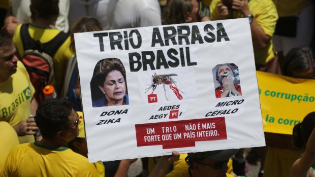 A man holds a poster showing images of Dilma Rousseff, an Aedes aegypti mosquito and Mr Lula with a message that reads "Trio Razes Brazil. A Trio is Not Stronger Than A Country", during a protest in Brasilia this month.
