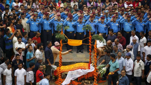 Nepali police officers salute as people watch  Laxman Neupane's son (right) cremate his father.