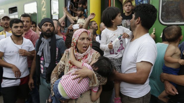 A woman carrying a child stands outside a train with migrants that was stopped in Bicske, Hungary, on Thursday.