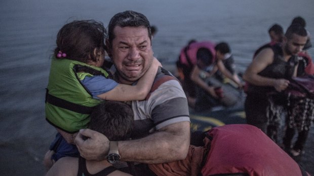 A Syrian refugee from Deir Ezzor, holding his son and daughter, breaks out in tears of joy after arriving via a flimsy inflatable boat crammed with about 15 men, women and children on the shore of the island of Kos in Greece.