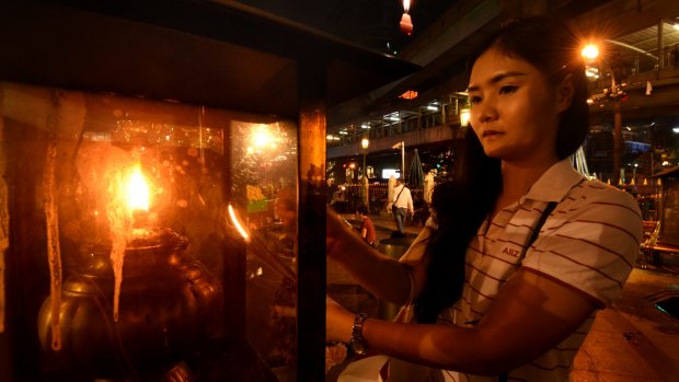 A young woman lights a candle before praying at Erawan Shrine in Bangkok on Thursday. 