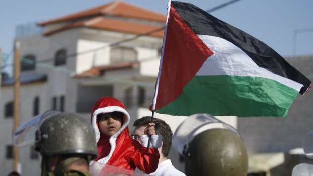 A Palestinian child dressed as Santa Claus holds a Palestinian flag in front of Israeli border police at a demonstration against a separation barrier in the West Bank village of Al-Masara in 2013.