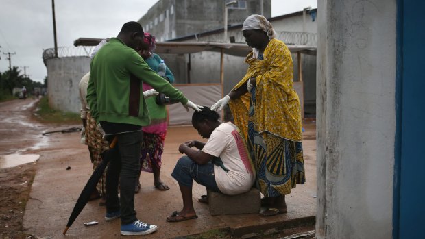 Family support: Relatives pray over Siata Johnson, 23, outside an Ebola treatment centre in Monrovia, Liberia.