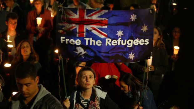 People hold candles and signs up in support of refugees.