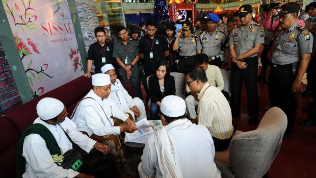 Police look on at a Surabaya shopping centre as centre staff sign a document provided by the Islam Defenders' Front promising not to dress employees in Christmas apparel.