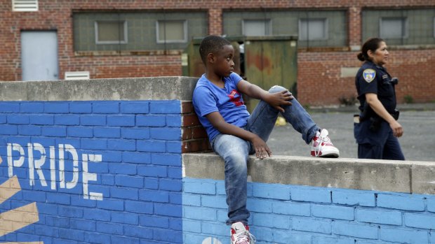 A boy sits on a wall as a Baltimore police officer walks by  near the site of unrest following the funeral of Freddie Gray. 