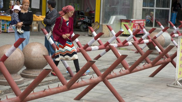 Uighur women walk past barricades set up at the entrance to a shopping district in the city of Aksu in western China's Xinjiang province in 2014.
