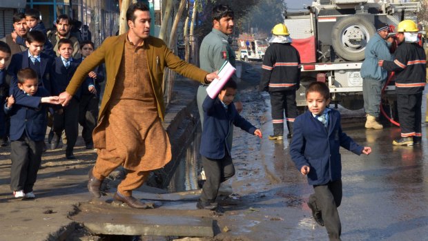 An Afghan teacher, in brown, helps school children run from the site of clashes near the Pakistan consulate in Jalalabad, capital of Nangarhar province, Afghanistan on Wednesday.