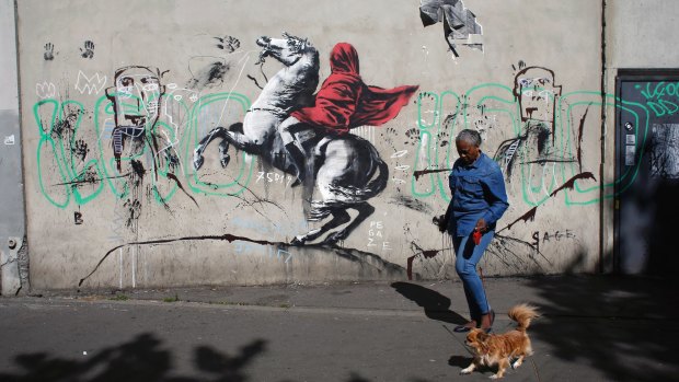 A woman walks past a graffiti attributed to street artist Banksy.