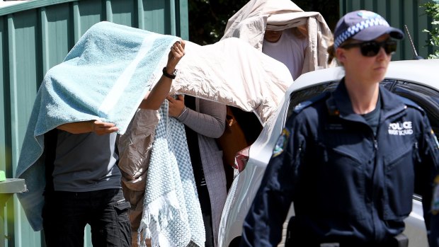 People covered in sheets and towels are escorted from a house during police raids on Wednesday.