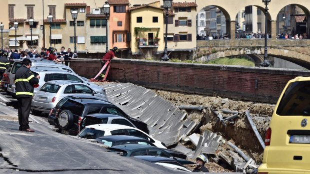 Firefighters standby by cars engulfed by a chasm which opened along the Arno River.