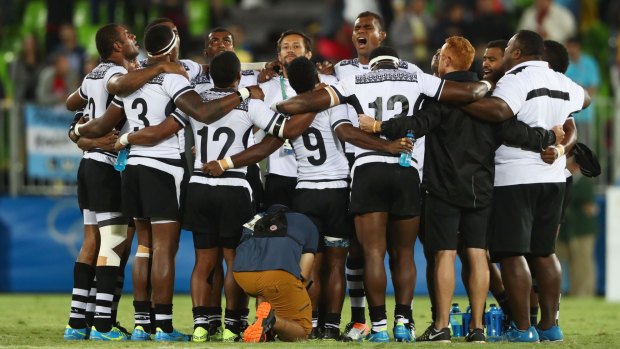 Fiji players and staff huddle together in celebration after winning the rugby sevens.
