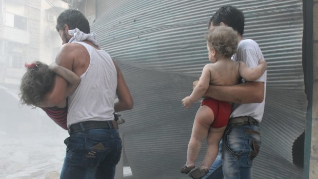 Syrians carry their children after the Syrian army carried out air strikes in Aleppo, Syria on August 13.