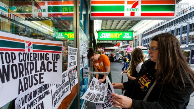 Protesters from the Young Workers Centre pin signs to the windows of 7-Eleven at a protest on Wednesday.