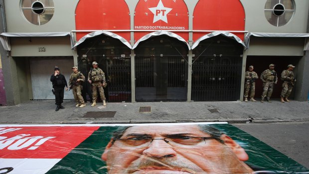 Federal police stand guard outside the headquarters of the Worker's Party (PT) next to a banner blanketing a street featuring Eduardo Cunha.