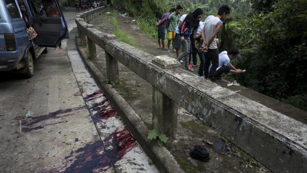 Blood stains the roadside as  civilians view unidentified bodies believed to have been executed and dumped in a ditch by militants. 