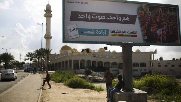 Boys sit under a billboard for the Joint List promising "one voice" next to a mosque at Rahat in southern Israel.