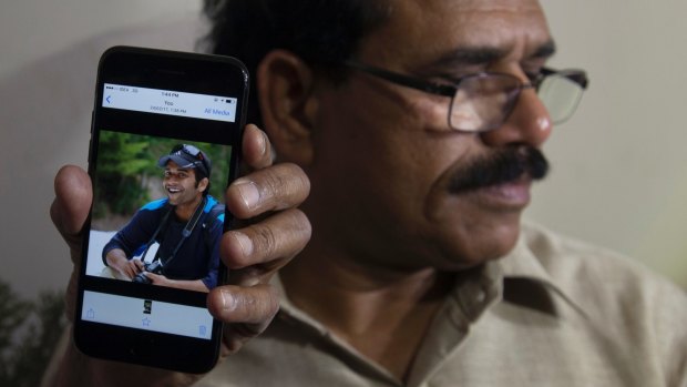 A man shows a picture of Alok Madasani, as his father Jaganmohan Reddy talks to the media in Hyderabad, India.