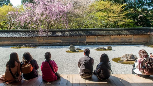 Japanese tourists enjoy tranquility at Ryoanji Temple. This Zen Buddhist temple is famous for its rock garden.