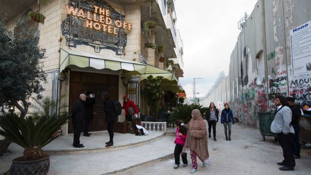 People pass the Walled Off Hotel and the wall in Bethlehem, in the Israeli-occupied West Bank.