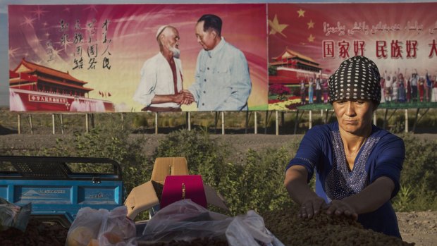 An ethnic Uighur woman arranges raisins for sale in Turpan County, Xinjiang. Behind her a billboard shows the late Communist Party leader Mao Zedong.