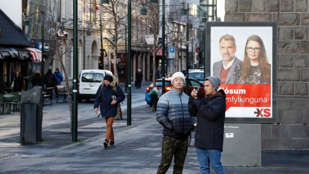Icelanders walk past a social democrats election poster in Reykjavik, Iceland on Thursday.