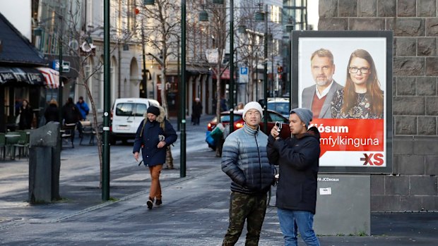 Icelanders walk past a social democrats election poster in Reykjavik, Iceland on Thursday.