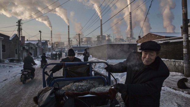 "China's Coal Addiction" by  Kevin Frayer show men pulling a tricycle in a neighborhood next to a coal-fired power plant in Shanxi.