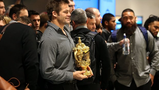 Richie McCaw keeps the World Cup trophy close as the All Blacks touch down in Auckland on Tuesday morning.