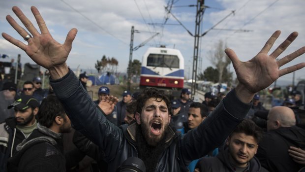 A refugee pleads with other men to calm down as a train attempts to pass at the Greek-Macedonia border in Idomeni, Greece. 