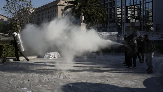 A protester sprays a fire extinguisher at riot police during a rally in front of the Athens University, on Thursday. 