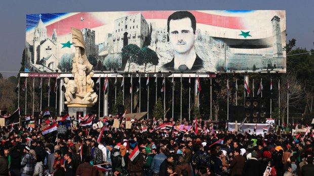 Pro-government supporters hold up the national Syrian flag and pictures of Syrian President Bashar al-Assad.