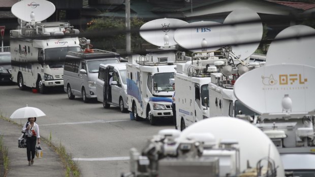 A woman walks by a line of outside broadcasting vans parked near the Tsukui Yamayuri-en facility.