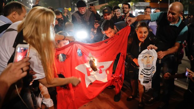Demonstrators set fire to a Workers Party flag and hold a doll of former President Luiz Inacio Lula da Silva in prison garb.