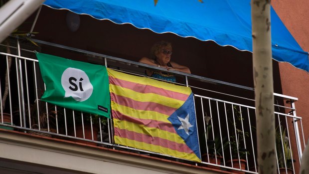 A woman looks out from her balcony decorated with an Estelada or pro-independence Catalan flag and a banner calling for a Yes vote. 