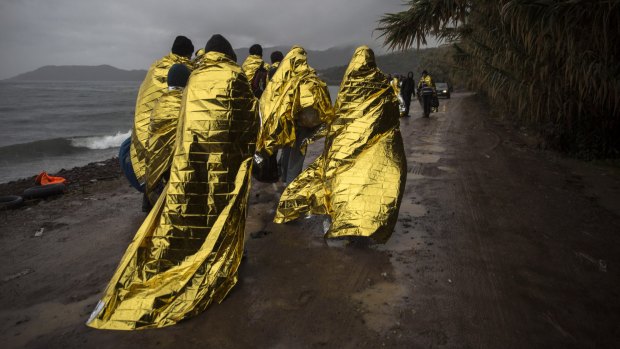 Refugees and migrants over themselves with thermal blankets after their arrival on a dinghy from the Turkish coast to the north-eastern Greek island of Lesbos.