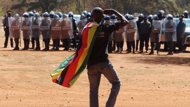 Riot police watch a man saluting with a Zimbabwean flag over his shoulders during a protest in Harare in August.
