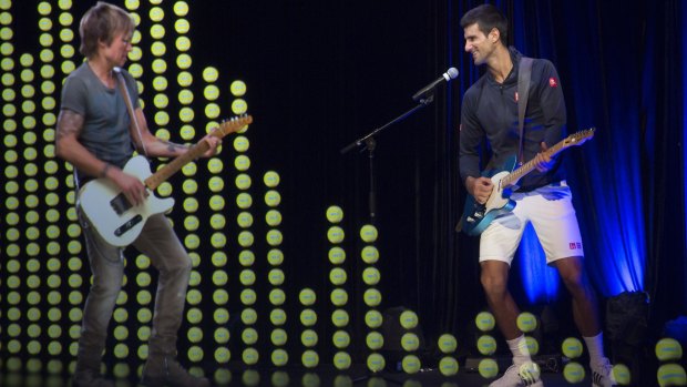 Novak Djokovic plays a guitar while standing alongside a hologram of Australian musician Keith Urban on Sunday.