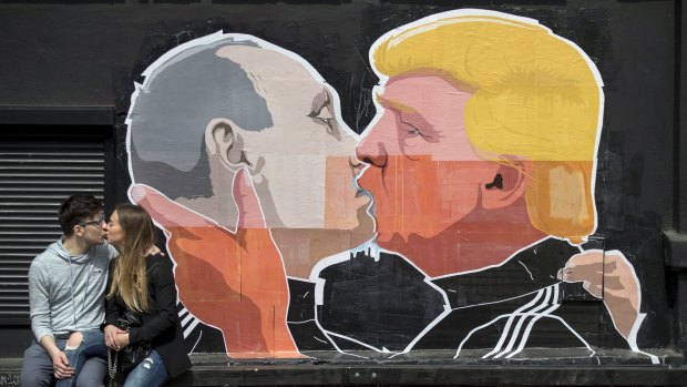 A couple kisses in Vilnius, Lithuania, alongside the mural of Vladimir Putin and Trump.