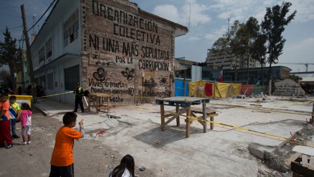 Students look at the site of a textile factory that collapsed in the 7.1 magnitude earthquake in Mexico City, last month. The mural reads in Spanish "Not one more to be buried by corruption.".