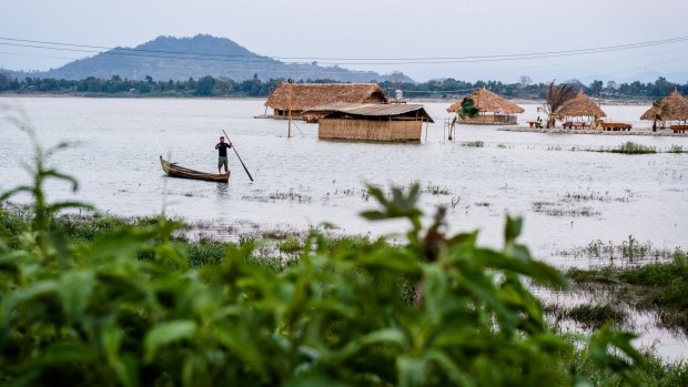 A man fishes from a small boat near a floating restaurant on the Irrawaddy River. 