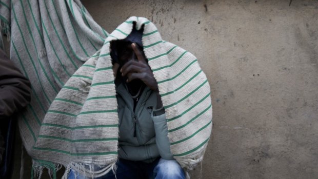 A migrant from Sudan shelters from the rain as he waits by the road in Calais, France, on Tuesday, after he travelled from the Mediterranean hoping to seek asylum in Britain.