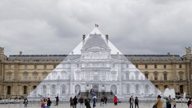 Tourists walk around the JR project at the Louvre Pyramid in Paris, on Tuesday.