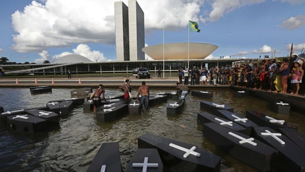Indigenous protesters from various ethnic groups place fake coffins, representing indians killed over the demarcation of land, in a water feature outside Brazil's National Congress.