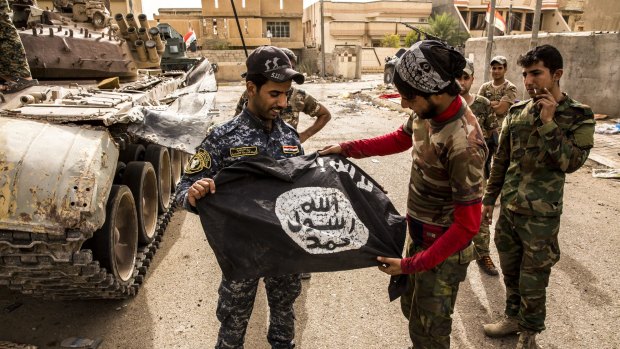 A member of the Iraqi federal police, left, and forces loyal to the Iraqi government displayed a captured Islamic State flag in the Nazal district of Fallujah.