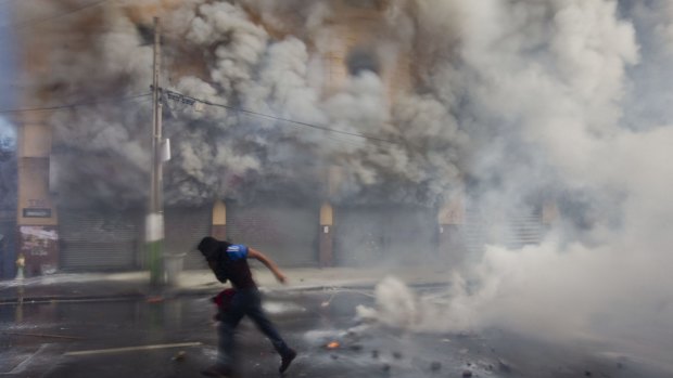 A masked protester runs from police responding with tear gas and water cannons in Valparaiso, Chile, on Saturday.