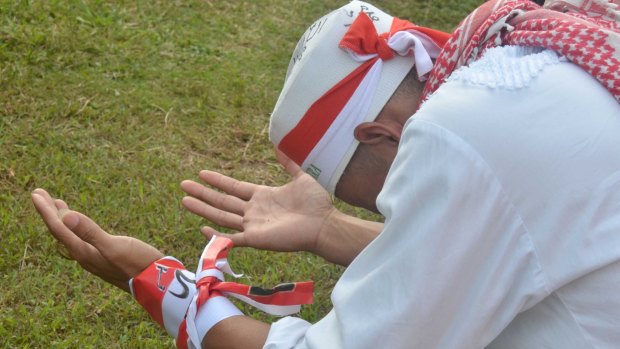 A man wearing Indonesian flag colours and Islamic symbols prays at an anti-Ahok rally.