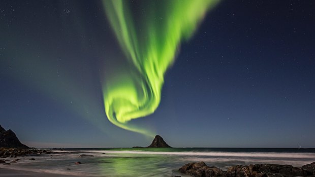 The green band of Auroras seem like smoke from the top of the rock.